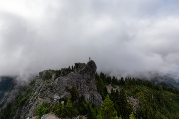 Adventurous Man Standing on top of a rugged rocky mountain during a cloudy summer morning. Taken on Crown Mountain, North Vancouver, BC, Canada.