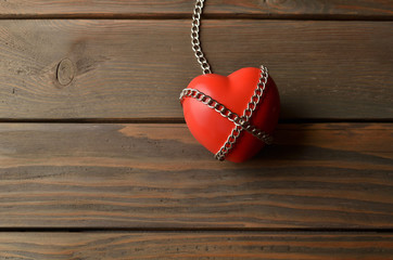 Heart and secured with the chain. Heart in chains on a dark wooden background. Red heart and secured with chains on a brown rustic table.