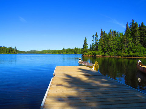 Canadian rabaska canoe resting by the calm water in beautiful  Wapizagonke lake. Mauricie National Park, Quebec Canada.Look out point with blue sky and tranquil waters landscap