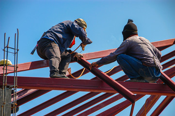 Construction worker men  welding roof steel beams, working on roof house