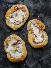 Puff pastry, ham, mozzarella cheese breakfast pizza on a dark background, top view
