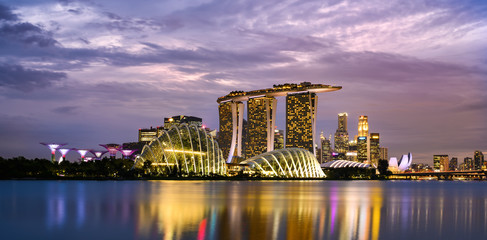 Stunning view of the illuminated skyline of Singapore during a dramatic sunset in the background and a calm bay in the foreground. Singapore is an island city-state of southern Malaysia.