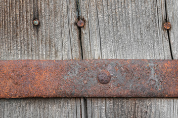 Wooden background from a fragment of an old wooden door with rusty door hinges and iron nails.