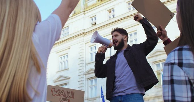 Handsome Caucasian young man, social activist saying his speech in the megaphone in front of the big crowd at the demonstration. Outside.