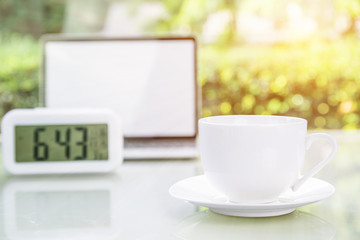 Coffee cup and laptop at office with digital clock
