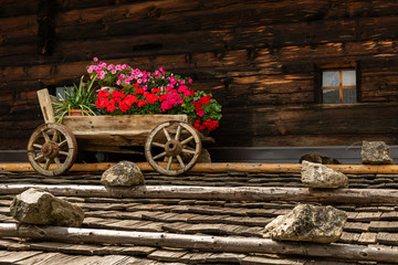 Obraz premium An old wooden cart with beautiful flowers on the roof of an old house