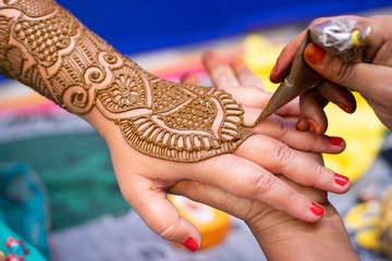young woman mehendi artist painting henna on bride's hand before wedding day