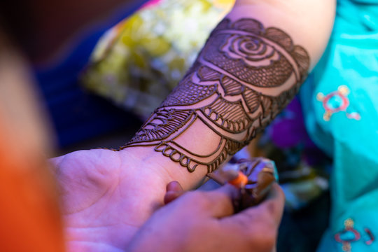 young woman mehendi artist painting henna on bride's hand before wedding day