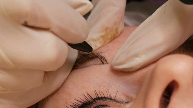 Microblading eyebrow tattoo, permanent makeup. A master in gloves, using special needle, injects pigment into the skin and stains the eyebrows using hair technique, making them natural, close-up view