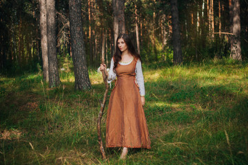 Young beautiful girl in medieval cowboy clothes, with a stick in hand. Barefoot on the ground....