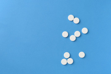 White round pills scattered on a blue background, top view. Medical pharmacy concept