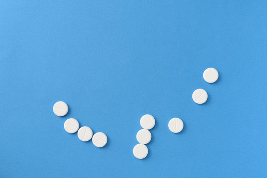White round pills scattered on a blue background, top view. Medical pharmacy concept