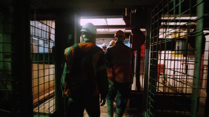 Silhouettes of workers with helmets and equipment leave the elevator leading to the mine. Miners go from work shift. 