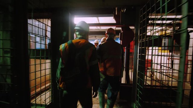 Silhouettes of workers with helmets and equipment leave the elevator leading to the mine. Miners go from work shift. 
