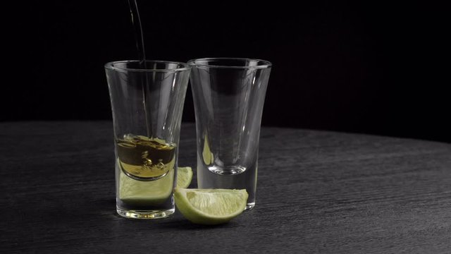 tequila is poured into two glasses on black background