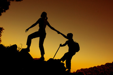 Obraz premium silhouette of two people climbing on the mountain and one people helping the other to go forward over sunset sky background