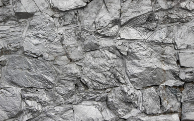 Wall made of natural rocks with decorative concrete borders painted with metallic silver paint