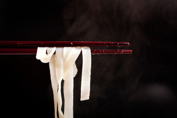 Udon noodles on chopsticks on black background with steam