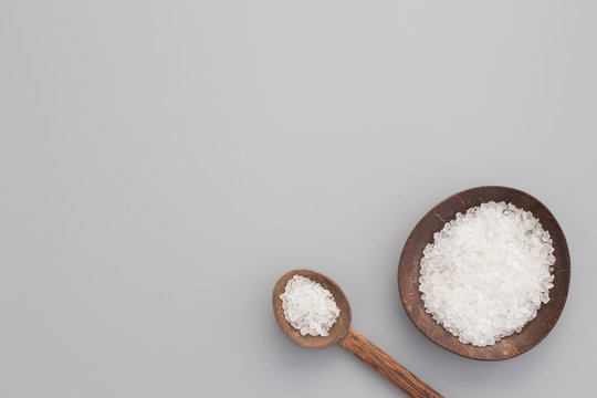 White bath salt in bowl and spoon from coconut shell on gray background. Natural spa products concept. Top view, flay lay, copy space