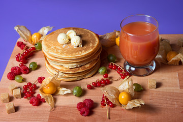 A stack of pancakes with icing sugar and a glass of juice on the table.