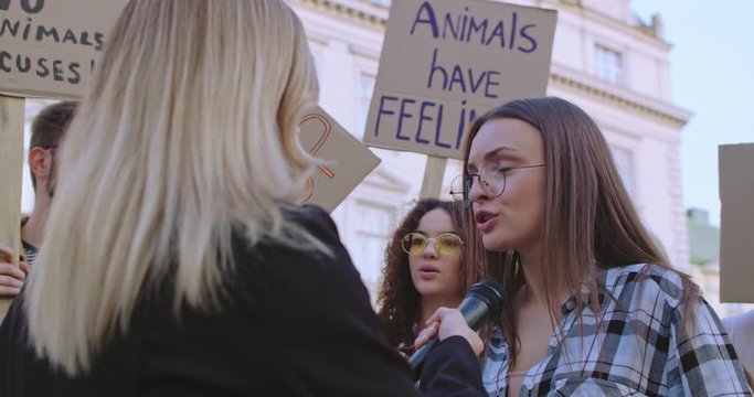 Rear of the blond Caucasian female journalist interviewing young student girl, social activist for animals rights and safe environment at the march. Back view.