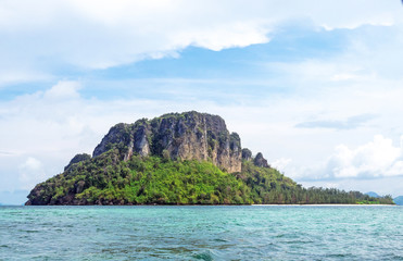 The tree mountain on the island in the middle of sea have blue sky and white cloudy. there are tourists far away.At krabi Thailand.