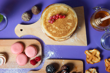 Pancakes with honey and sweets on a purple background, top view.