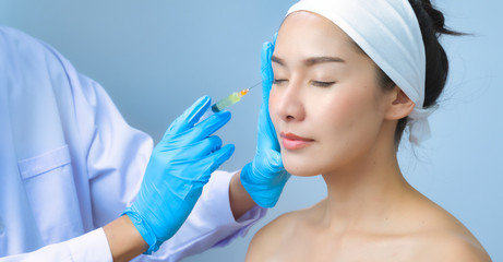 Naklejka premium Asian young woman gets injection in her lips. Woman in beauty salon. plastic surgery clinic.Beautiful woman gets injection in her face.