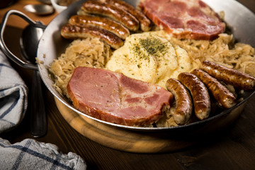 Sauerkraut Pfanne mit Nürnberger Rostbratwürste, Kassler Nacken,  Kartoffelpüree und Senf auf Holz Tisch