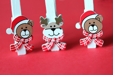 Funny wooden clothespins with wild animals on red background. Bears and deer in red hats and checkered scarfs. New Year and Christmas festive backdrop. Greeting card, poster template
