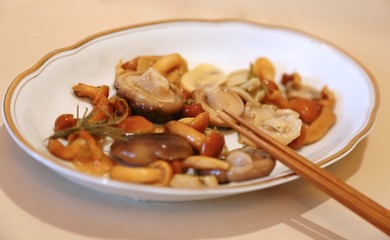 Mushrooms are small salty in sauce wet on a plate of white and sticks for eating 
