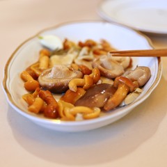 Mushrooms are small salty in sauce wet on a plate of white and sticks for eating 