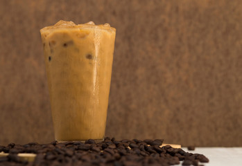 A glass of iced coffee with coffee beans on table and brown wooden background with space