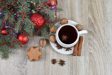 White cup with black tea on the christmas tree phoenias on a wooden table. Red balls. Vanilla, nuts, anise. Spicy cookies.