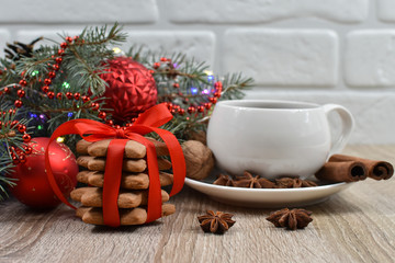 White cup with black tea on the christmas tree phoenias on a wooden table. Red balls. Vanilla, nuts, anise. Spicy cookies.