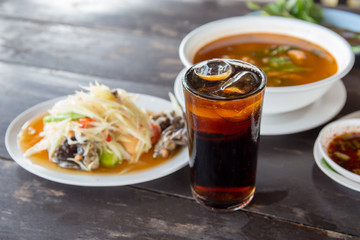 Pop water or cola in glass with ice cubes with food in the background.
