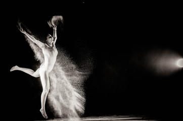 Obraz na płótnie Canvas The girl with the flour on the body stretches the arms up with thrown flour on black background black and white image