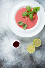Cream-soup with fresh strawberries served in a white plate, above view over light-grey stone surface with space