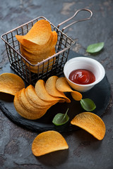 Potato chips with paprika on a stone slate, vertical shot on a brown stone background