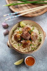 Bowl of rice with meatballs cooked in panasian style, vertical shot over beige stone background