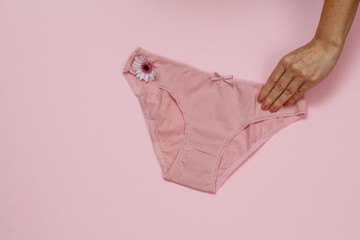 Women's hand with beautiful panties on pink background.