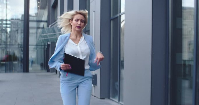 Good looking young Caucasian businesswoman going to work in the morning, lookig at watch on hand and running as being very late at the business meeting.
