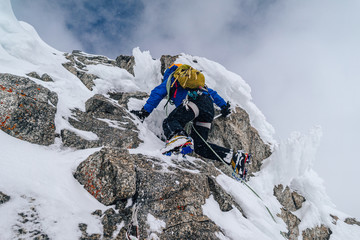 An alpinist climbing an alpine ridge in winter extreme conditions. Adventure ascent of alpine peak in snow and on rocks. Climber ascent to the summit. Winter ice and snow climbing in mountains.