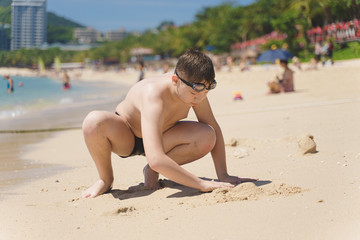 boy sitting on beach beyond sea and sculpting figures of sand by hands Hobby, leisure on summer vacation concept.
