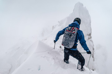Fototapeta na wymiar An alpinist climbing an alpine ridge in winter extreme conditions. Adventure ascent of alpine peak in snow and on rocks. Climber ascent to the summit. Winter ice and snow climbing in mountains.
