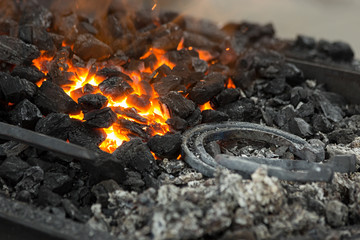 Horseshoe annealing in a portable forge brazier. Embers glow in a iron forge. Fire, heat, coal and ash.