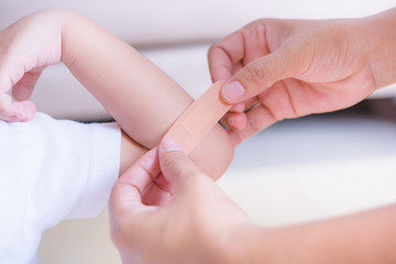 Fototapeta na wymiar Mother applying adhesive plaster bandage on childen arm wound