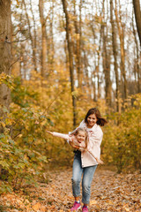 Happy mother playing with her little daughter in the autumn park and holding smiling girl in her arms