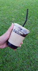  hand holding a Coffee paper cup witch green background.watering  in garden