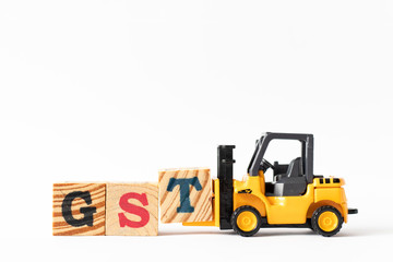 Toy forklift hold wood letter block T to complete word GST (Abbreviation of Goods and Service Tax) on white background